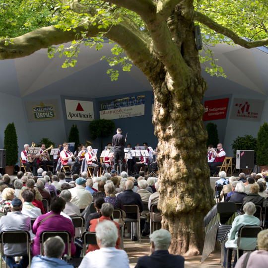 Das Volksparkkonzert im Blauen Pavillon ist gut besucht von Senioren und Seniorinnen. EIne Blumenpracht gibt dem Ganzen einen frühlingshaften Flair.