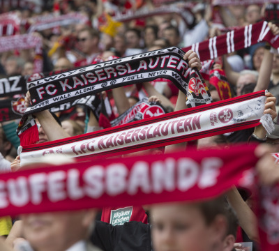 Nahaufnahme der Westtribüne im Fritz-Walter-Stadion. Man sieht FCK-Fans, die Fanschals hochhalten.