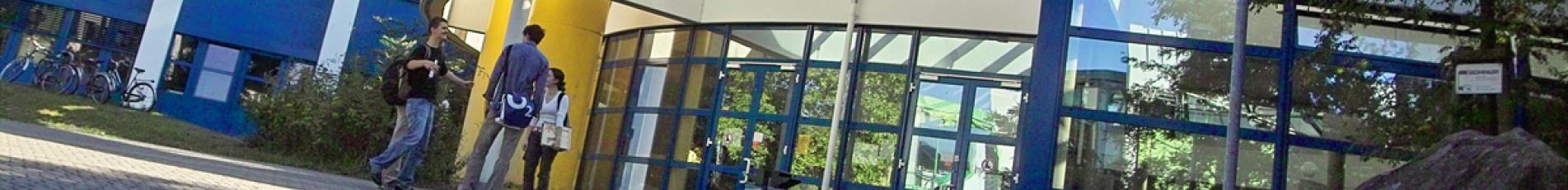 Eine Aufnahme von schräg unten auf der das helle Gebäude 42 zu sehen ist, dessen Fassade durch eine gläserne Glasfront im unteren und oberen Bereich ein einladendes und fortschrittliches Aussehen besitzt.