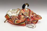 Eine japanische Puppe. Mit weißer Schminke, ausladender rötlicher Kleidung und einem Fächer.
