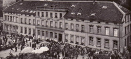 Eine Fotografie, die das alte Gebäude des Museums zeigt. Der Stiftsplatz vor dem Gebäude ist stark belebt, u.a. wegen den aufgebauten Marktständen.