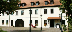 Der Wadgasserhof von außen. Rechts und links umrahmen grüne Hecken und Bäume das Bild.
