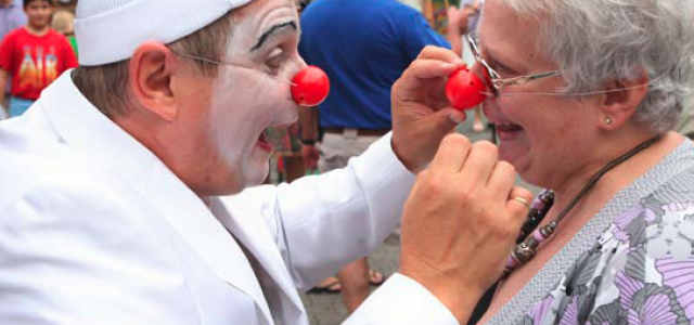 Ein Clown mit roter Nase setzt einer älteren Dame ebenfalls eine rote Nase auf. Diese nimmt es mit viel Humor.