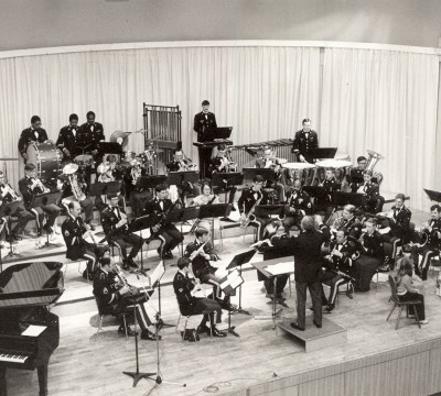 Eine schwarz-weiß Fotografie bei der die Big Band Mitglieder in Uniform spielen. Eine Erzählerin und ein Kind sind im Vordergrund beim Weihnachtsbaum zu sehen.