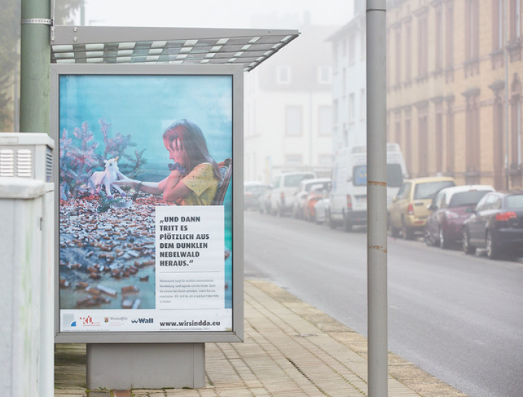 Bushaltestelle mit Plakat. Auf dem Plakat ist ein Kind in einem Berg von Zigarettenstummeln zu sehen, Kind hält ein Einhorn in der Hand. 