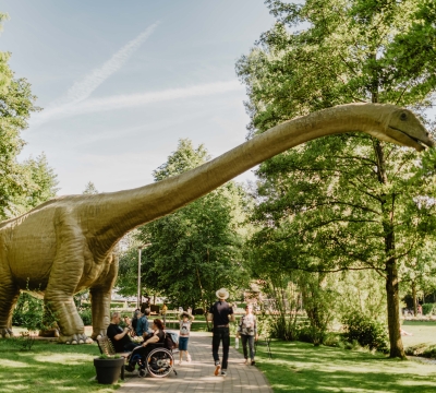 Thomas Linkel, Lizenz CC-BY Gelände der Gartenschau. Man sieht einen großen Dinosaurier, Menschen und viel Grün.