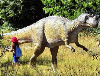 Mädchen mit rotem Hut streichelt Gartenschau-Dino im Vorbeigehen