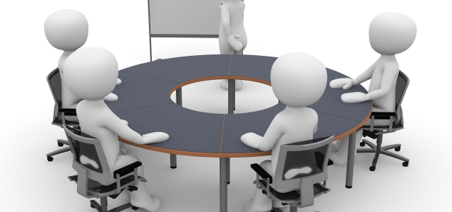 Piktogramm: Männlein am Tisch vor Flip-Chart mit dem Schriftzug Meeting.